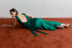 woman lying on red carpet wearing a green silk maxi dress with low cowl back