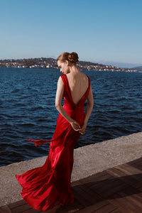 woman in red silk cowl back dress looking at the water ahead
