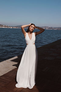 woman standing near water wearing white v neck pleated maxi dress